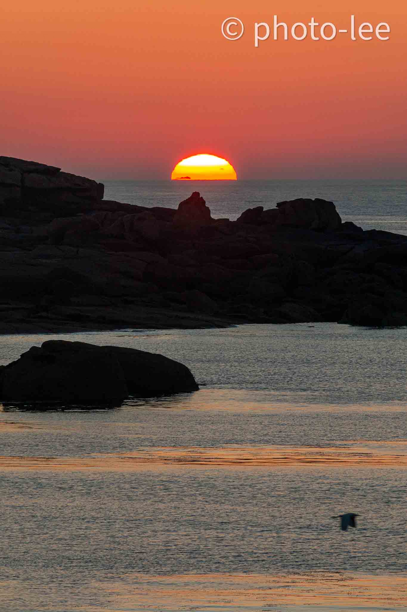 Die halbuntergegangene Sonne vor ein paar Felsen im Meer